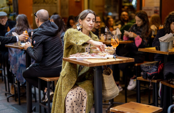 Woman sitting on crowded street at bar or restaurant outdoors